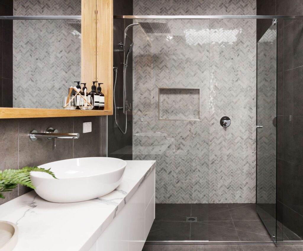 A small bathroom with grey tiles and a clear glass shower screen.