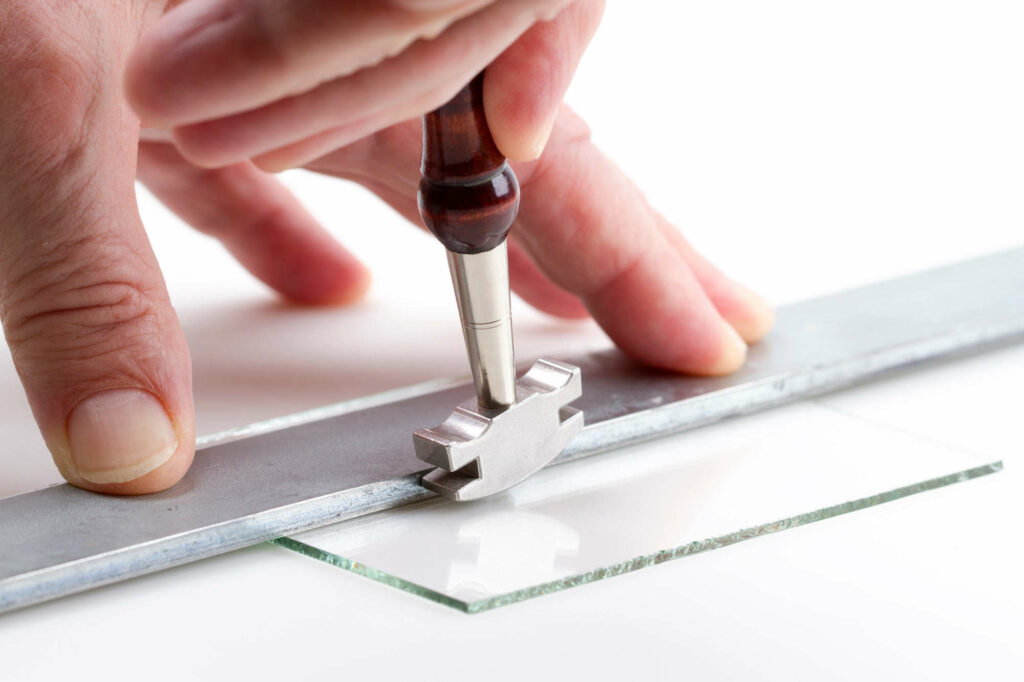 Person cutting a thin sheet of glass using a guide